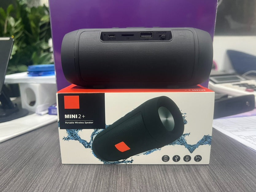 Black portable wireless speaker on top of its packaging box with a purple background